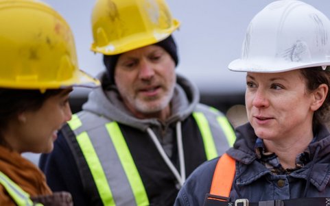 Deux ouvrières et un ouvrier discutant et portant un casque de chantier